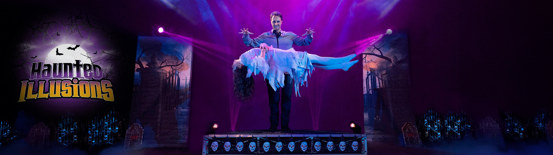 Magician levitates a woman in a ghostly white costume on a spooky stage with purple lighting, fog, skulls, and graveyard scenery.