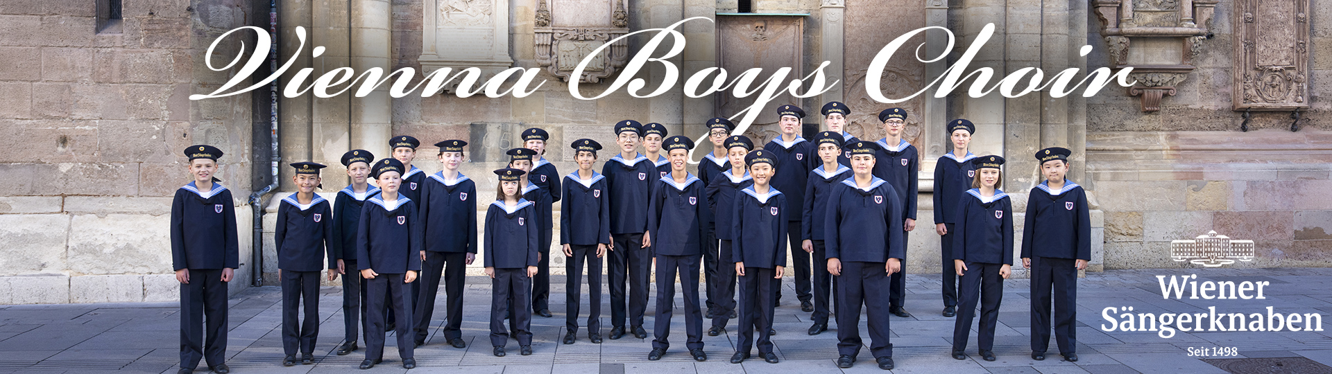 Vienna Boys Choir members in uniform standing outside a historic building with the Wiener Sängerknaben logo.