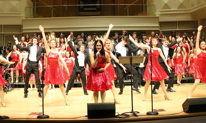 A vibrant performance featuring a group of singers in sparkly red dresses and black tuxedos, energetically engaging the audience on stage.